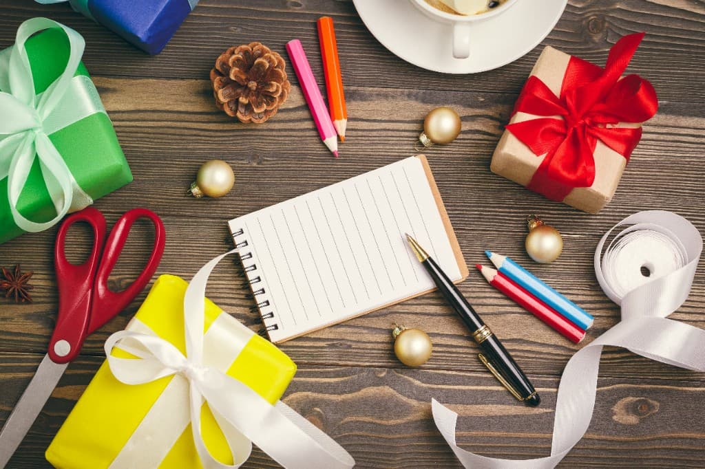 Creative craft workspace with wrapped gifts, ribbons, notebook, and tools on a wooden table