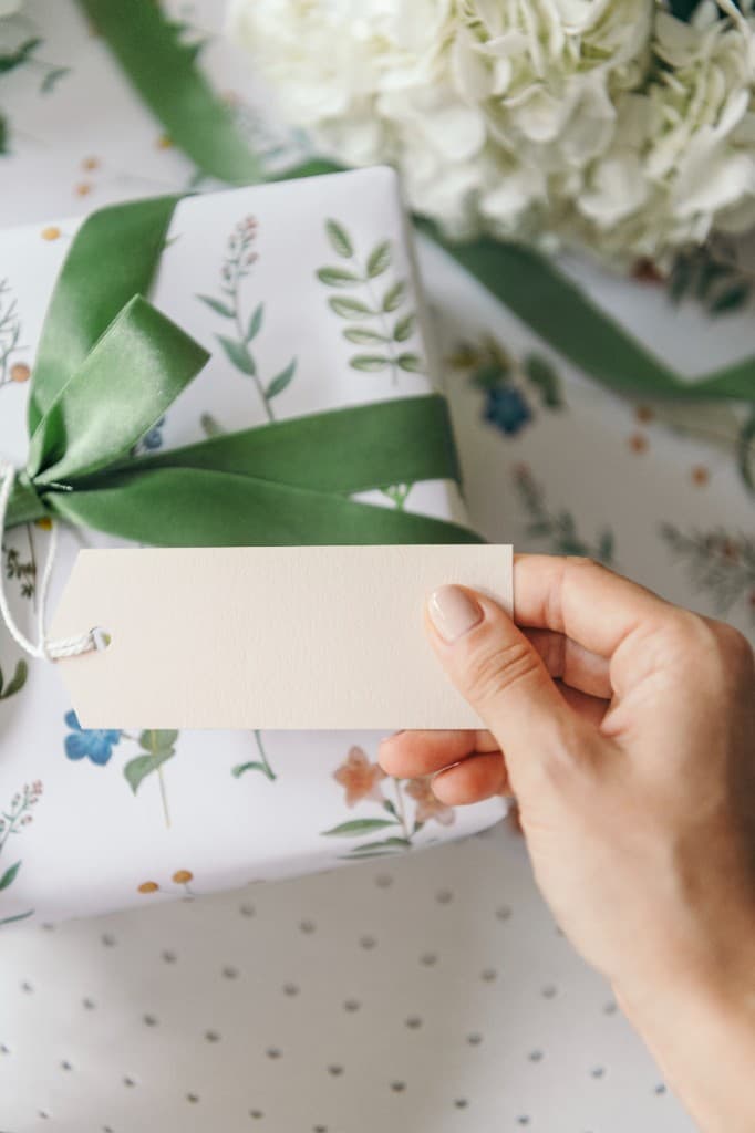 Hand holding a gift tag on a present wrapped in floral paper with a green bow